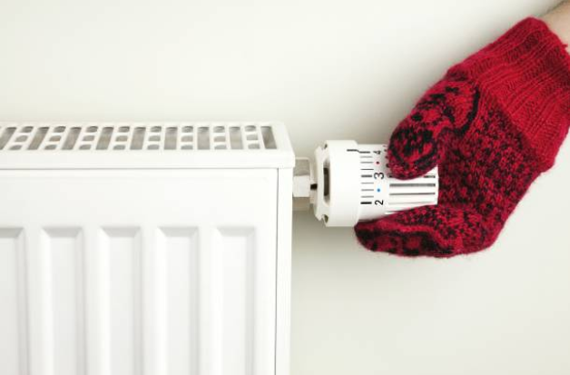 Main dans un gant en laine rouge qui règle la température d'un radiateur