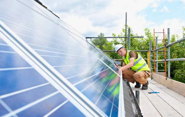 Homme en tenue de travail qui installe des panneaux solaires sur un toit