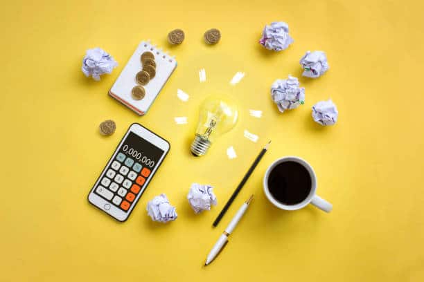 Ampoule vue de haut sur fond jaune avec téléphone portable, tasse de café, boules de papier et stylos autour