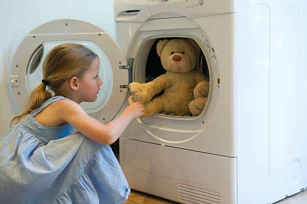 Petite fille en train de mettre son ours en peluche à la machine à laver