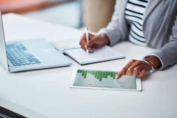 Femme en train de faire des calculs sur un carnet et à l'aide d'une tablette