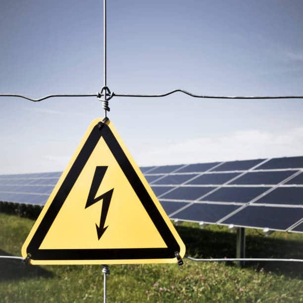 Panneau "danger" devant un champ de panneaux solaires photovoltaïques